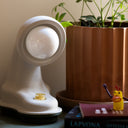 Lifestyle image of the Nessi table lamp in Putty next to a plant and some books.