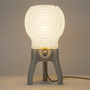 The glowing Visitor table lamp in Putty illuminates a room.