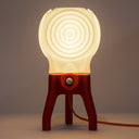 The glowing Visitor table lamp in Coral illuminates a dark room.