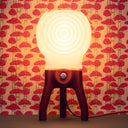 The glowing Visitor table lamp in Coral in front of mushroom wallpaper.
